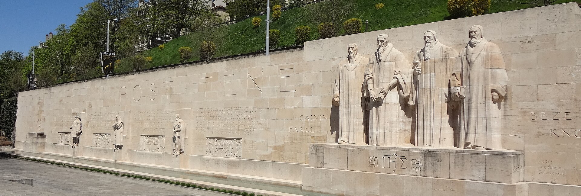 The four central reformers stand above a narrow water channel along Geneva's Reformation Wall, with inscriptions and relief panels.