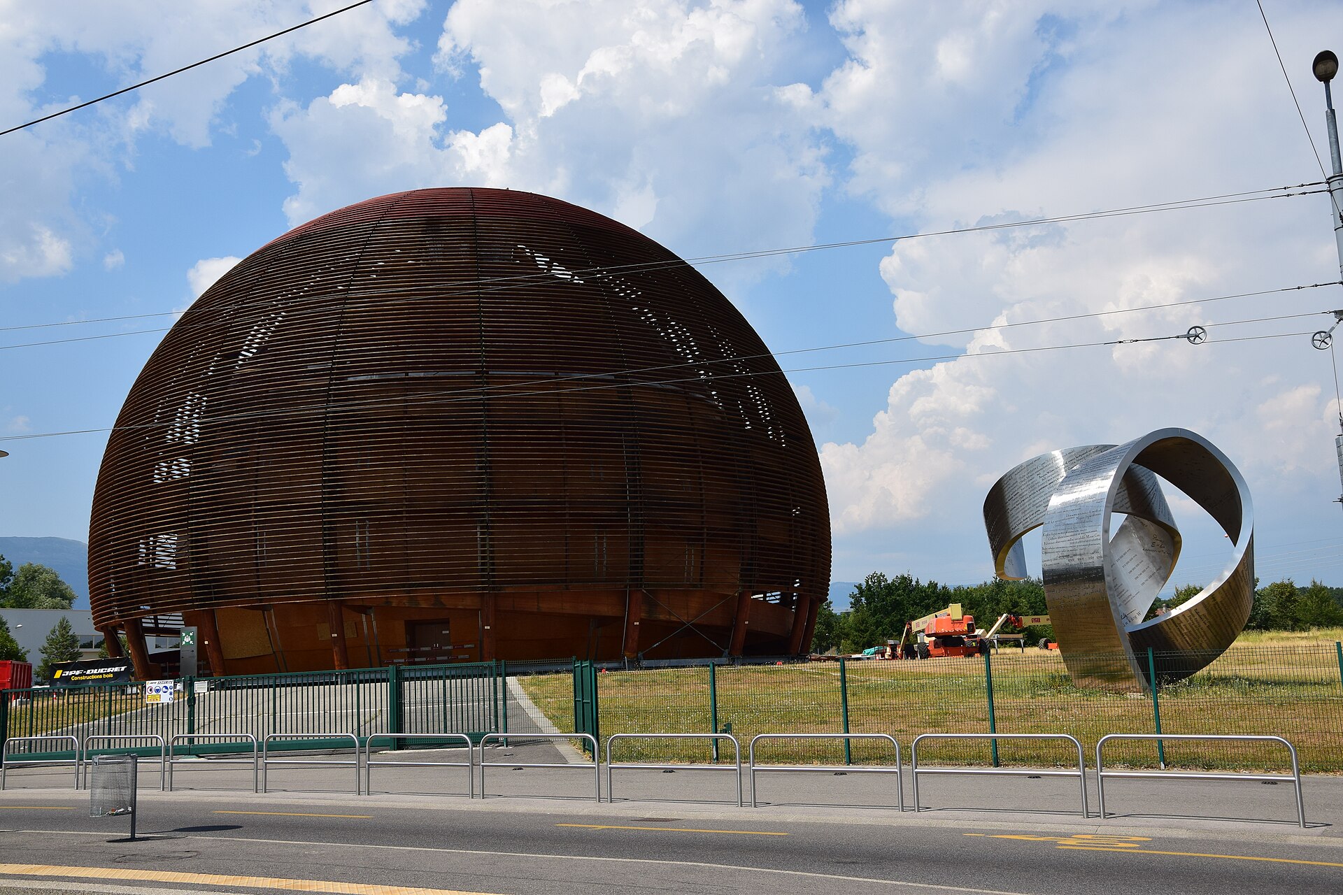 CERN's large wooden Globe of Science and Innovation at Meyrin, with a curved steel sculpture in front and a blue sky