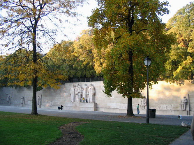 The long stone Reformation Wall in the Parc des Bastions in Geneva, seen across the lawn between trees with autumn leaves