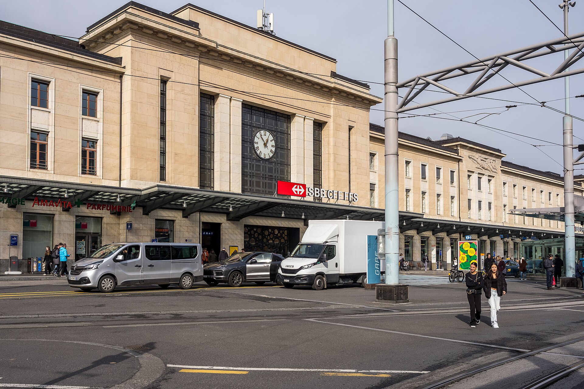 Geneva Cornavin station faces a busy forecourt beneath tram wires, with its clock and SBB lettering above the entrance.