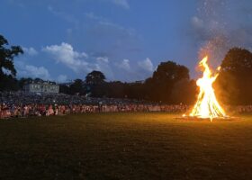 A large bonfire burning on the lawn of Parc La Grange in Geneva on 1 August 2024, with a crowd watching and the Villa La Grange behind at dusk