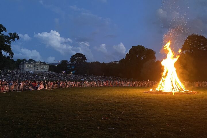 A large bonfire burning on the lawn of Parc La Grange in Geneva on 1 August 2024, with a crowd watching and the Villa La Grange behind at dusk