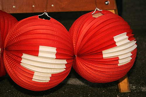 Two round red paper lanterns printed with the white Swiss cross hanging from a wooden stall