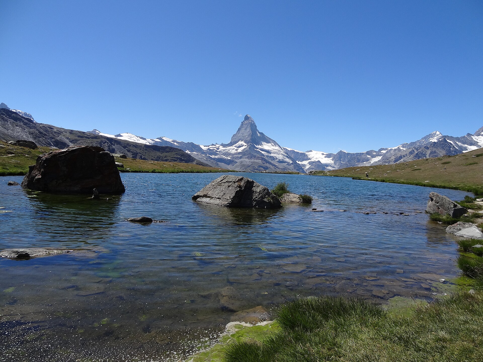 The Matterhorn above the still waters of the Stellisee near Zermatt in summer, with rocks in the lake and a clear blue sky