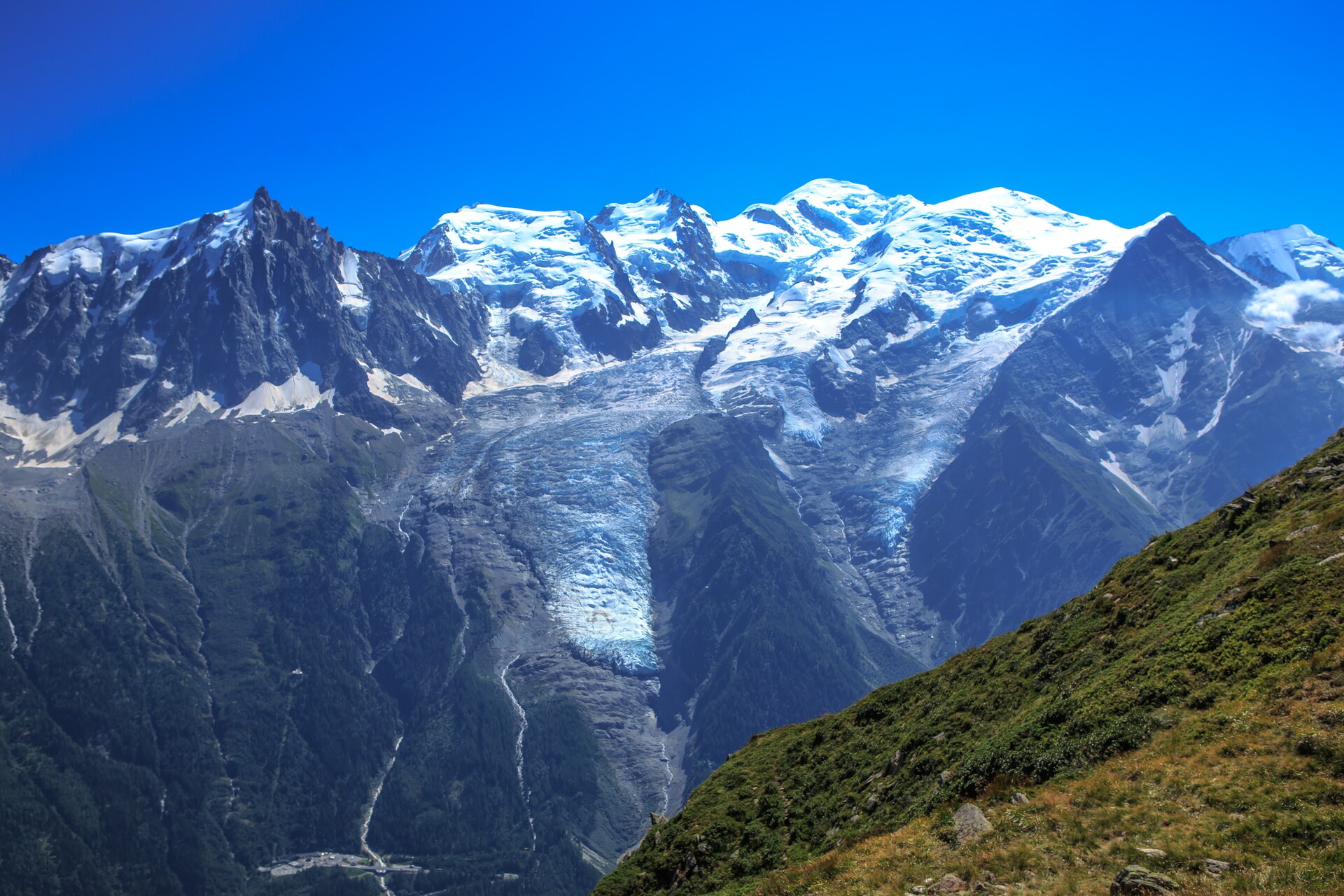 The snow-covered Mont Blanc massif and the Aiguille du Midi above the Chamonix valley in summer, seen from Le Brévent, with glaciers and green slopes