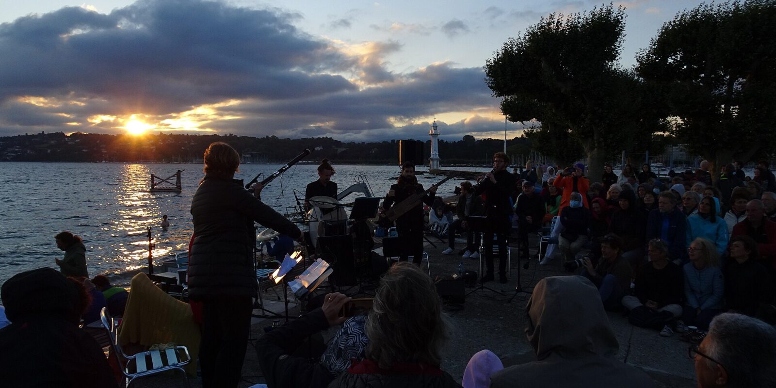 Sunrise over Lake Geneva from the jetty of the Bains des Pâquis during an Aubes Musicales concert, with musicians and a seated audience in silhouette