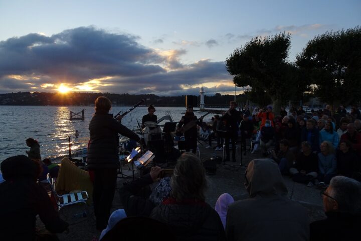 Sunrise over Lake Geneva from the jetty of the Bains des Pâquis during an Aubes Musicales concert, with musicians and a seated audience in silhouette