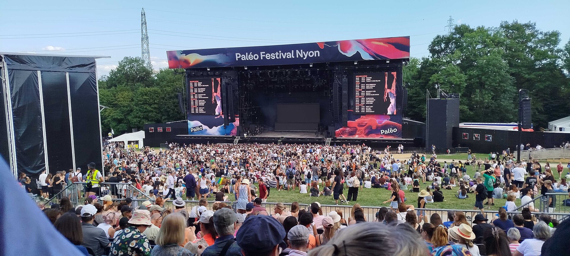 A large crowd on the grass in front of the main stage of the Paléo Festival in Nyon in 2026, with the festival banner above the stage