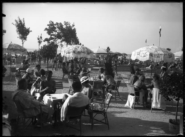 Black and white photograph of bathers at café tables under striped umbrellas on the lawns of Genève-Plage in August 1933
