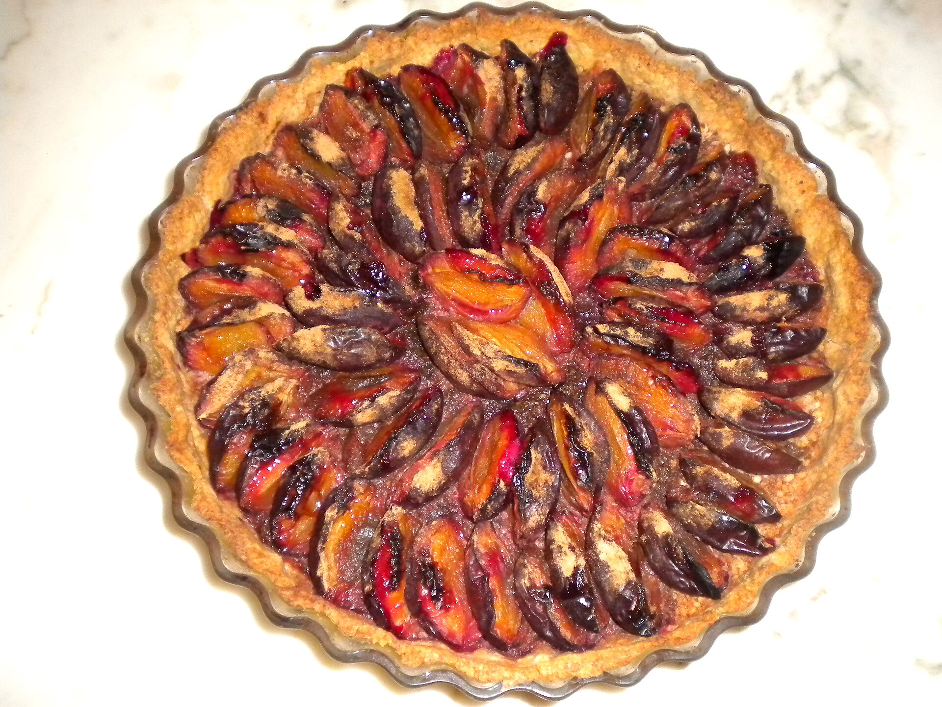 A round plum tart with halved plums arranged in a spiral, baked for the Jeûne genevois