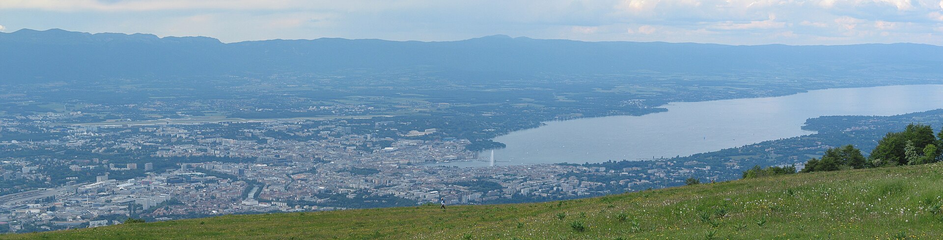 Geneva and Lake Geneva extend below a grassy Salève slope, with the Jet d'Eau visible near the waterfront.