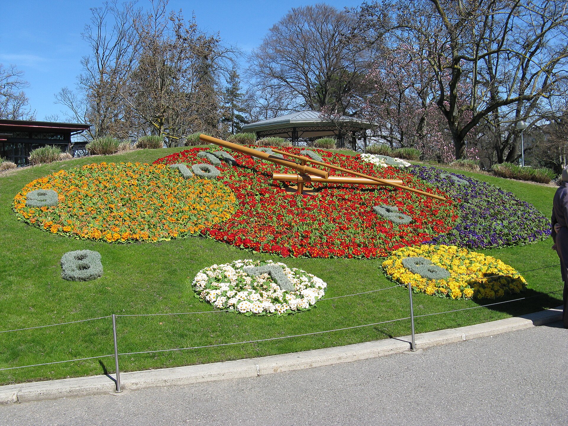 Geneva's Flower Clock planted with orange, red, white and yellow flowers, its long hands set across a sloping lawn.