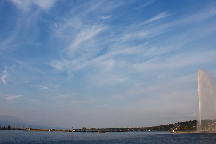 Geneva's Jet d'Eau rises above the harbour beneath wispy clouds in the evening sky.