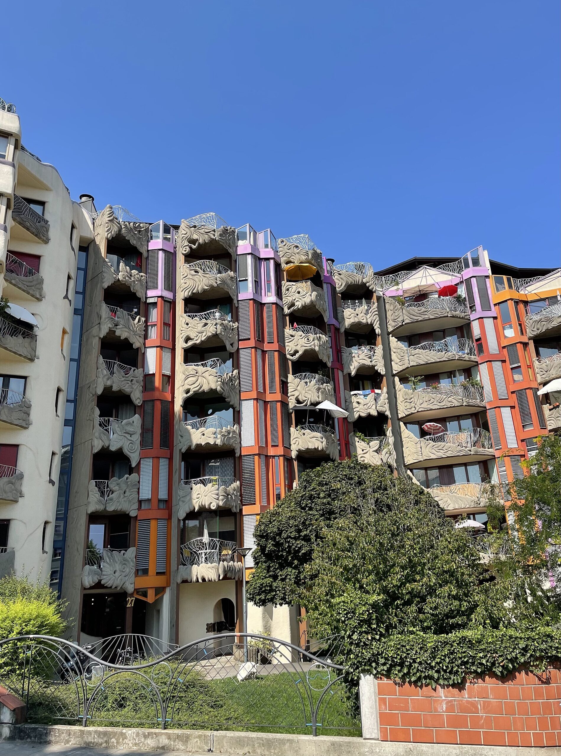Geneva's Schtroumpfs buildings display sculpted balconies and orange and purple window bays above a garden and wavy railings.