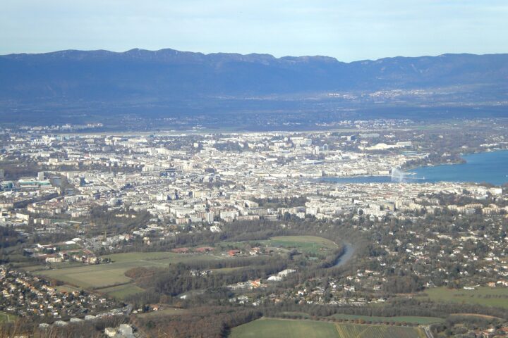 Green fields and the wooded Arve bend lead toward Geneva, Lake Geneva and the Jura in this Salève view.