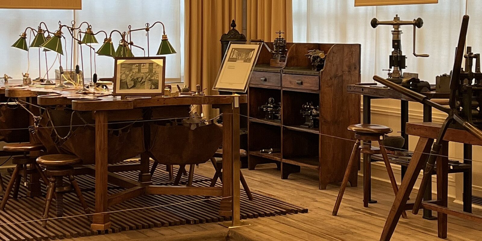 Green lamps illuminate watchmaking benches beside a tool cabinet and press inside Geneva’s Patek Philippe Museum.