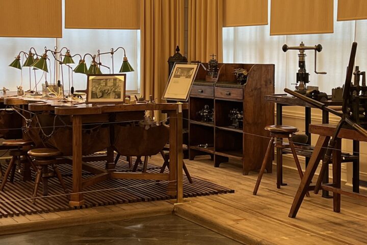 Green lamps illuminate watchmaking benches beside a tool cabinet and press inside Geneva’s Patek Philippe Museum.