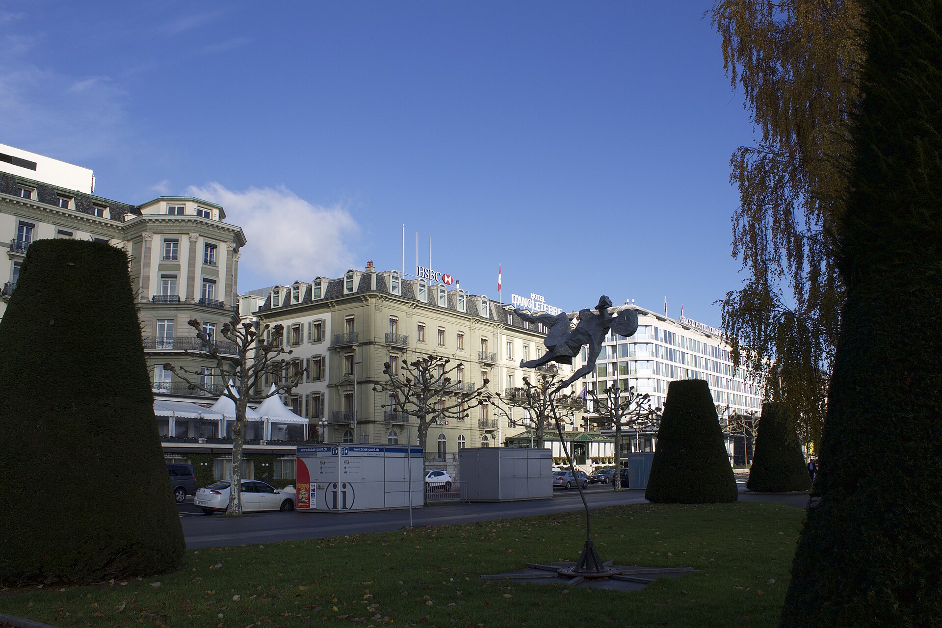 Hôtel d'Angleterre in Geneva behind pollarded trees, with its rooftop sign visible above the cream facade.