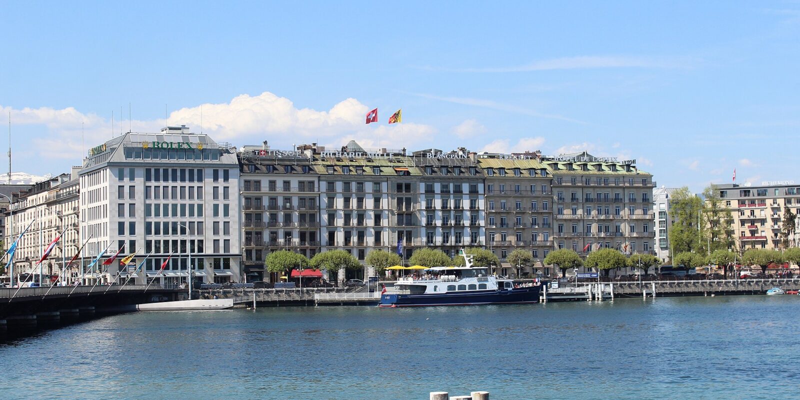 Hôtel de la Paix overlooks Geneva's Quai du Mont-Blanc, with a moored passenger boat and blue lake water in front.