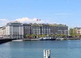 Hôtel de la Paix overlooks Geneva's Quai du Mont-Blanc, with a moored passenger boat and blue lake water in front.