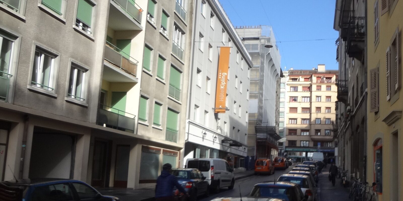 Hotel Kipling's orange sign overlooks Rue de la Navigation in Geneva, with parked cars and a cyclist passing.