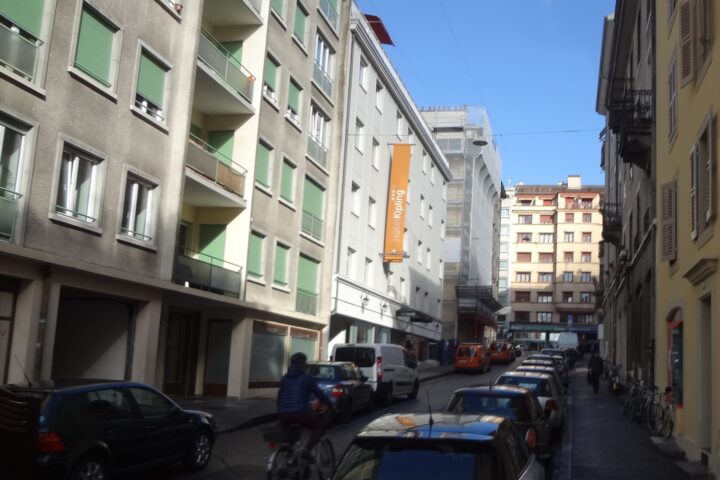 Hotel Kipling's orange sign overlooks Rue de la Navigation in Geneva, with parked cars and a cyclist passing.