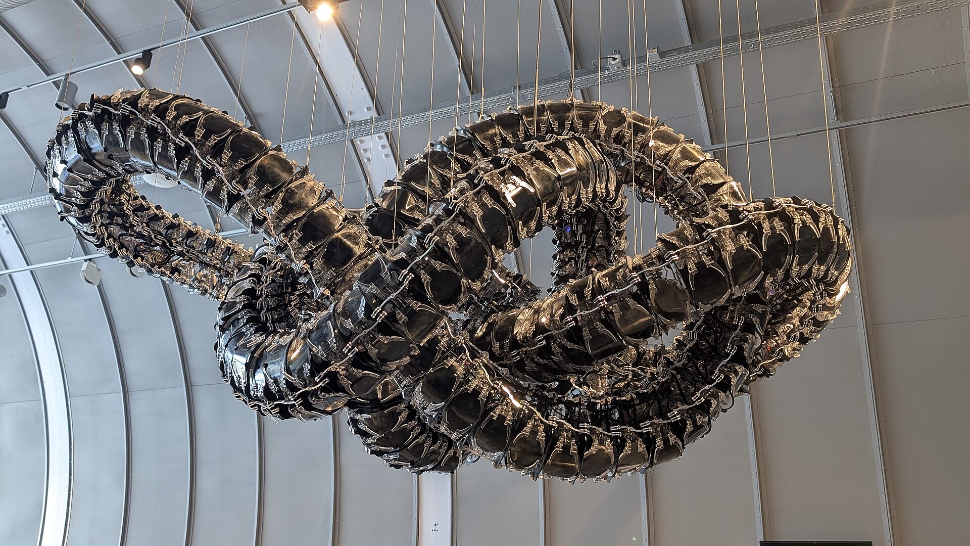 The looping Chroma VII installation hangs from cables beneath the curved exhibition pavilion roof at CERN Science Gateway in Meyrin.