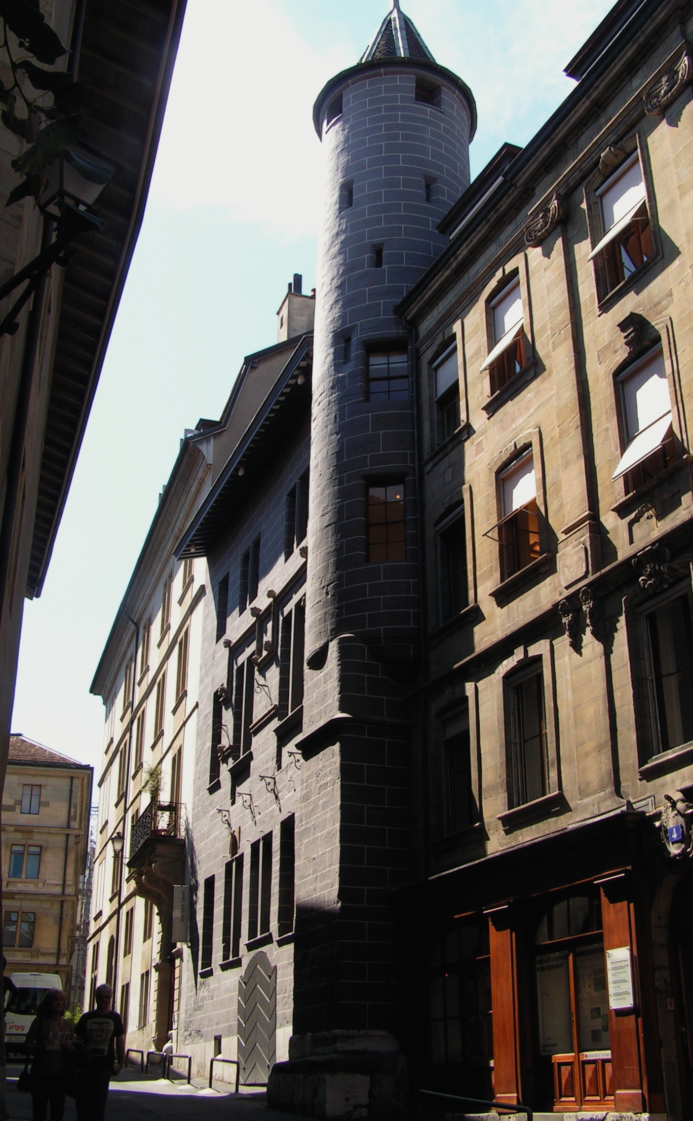 Maison Tavel's turret projects above a narrow Geneva Old Town street beside a yellow shuttered house.