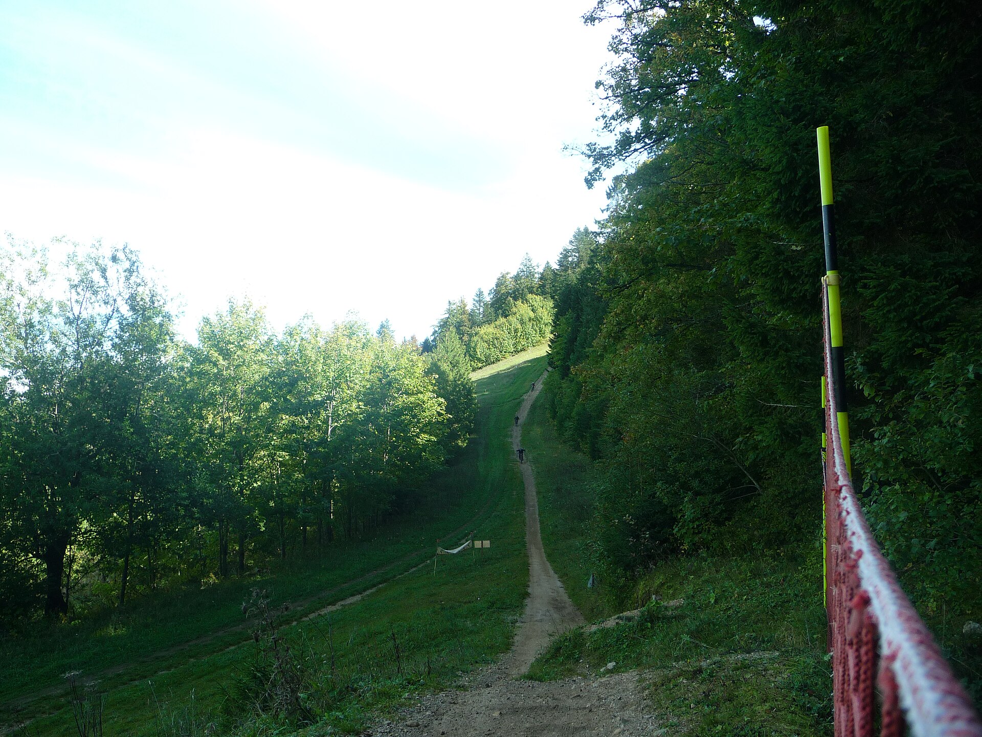 Mountain bikers descend a narrow dirt track through a grassy clearing between forested slopes at Métabief in the Jura.