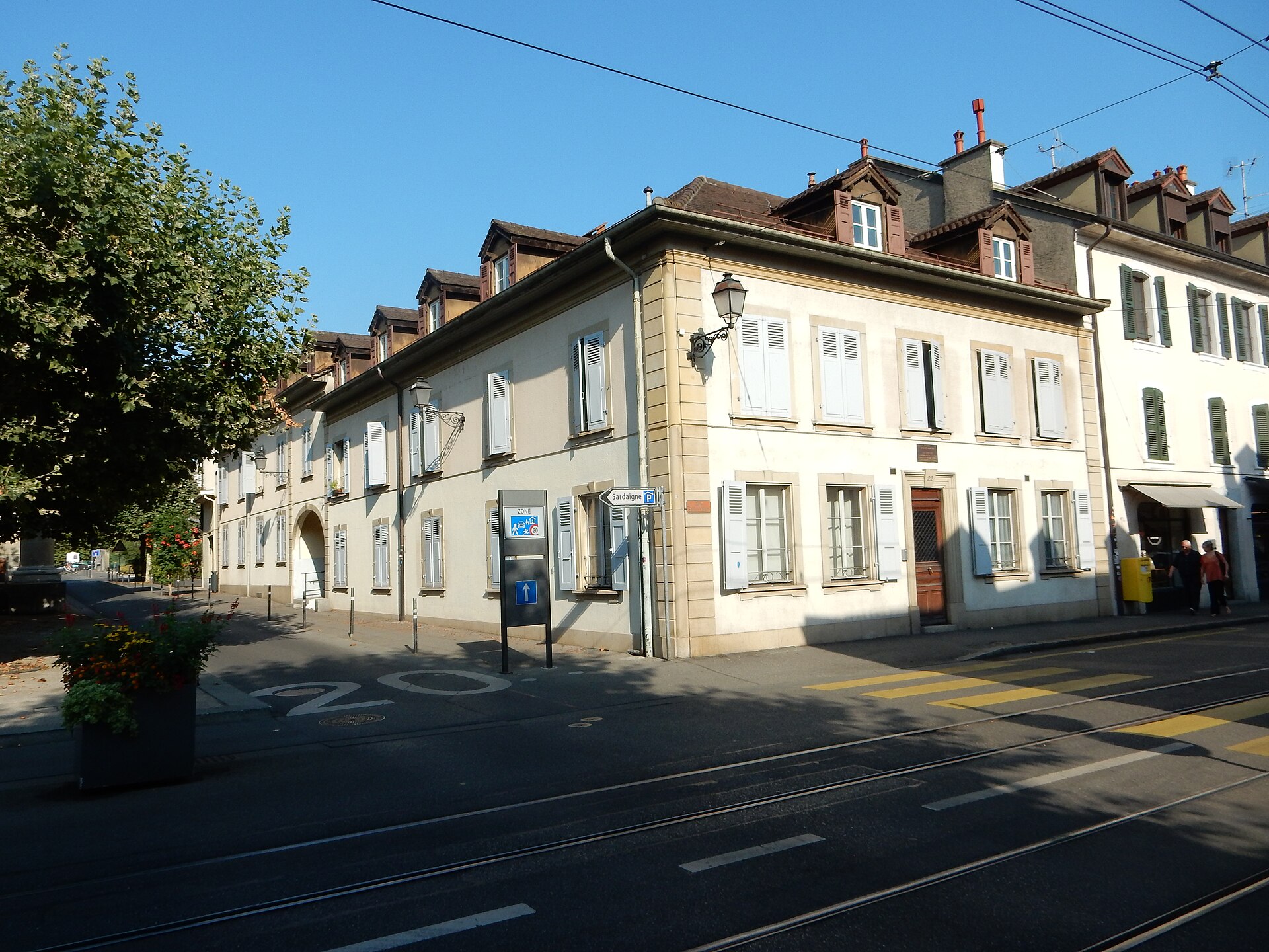 A pale yellow house with white shutters stands at 22 Rue Saint-Victor in Carouge, beside a tree-lined side street.
