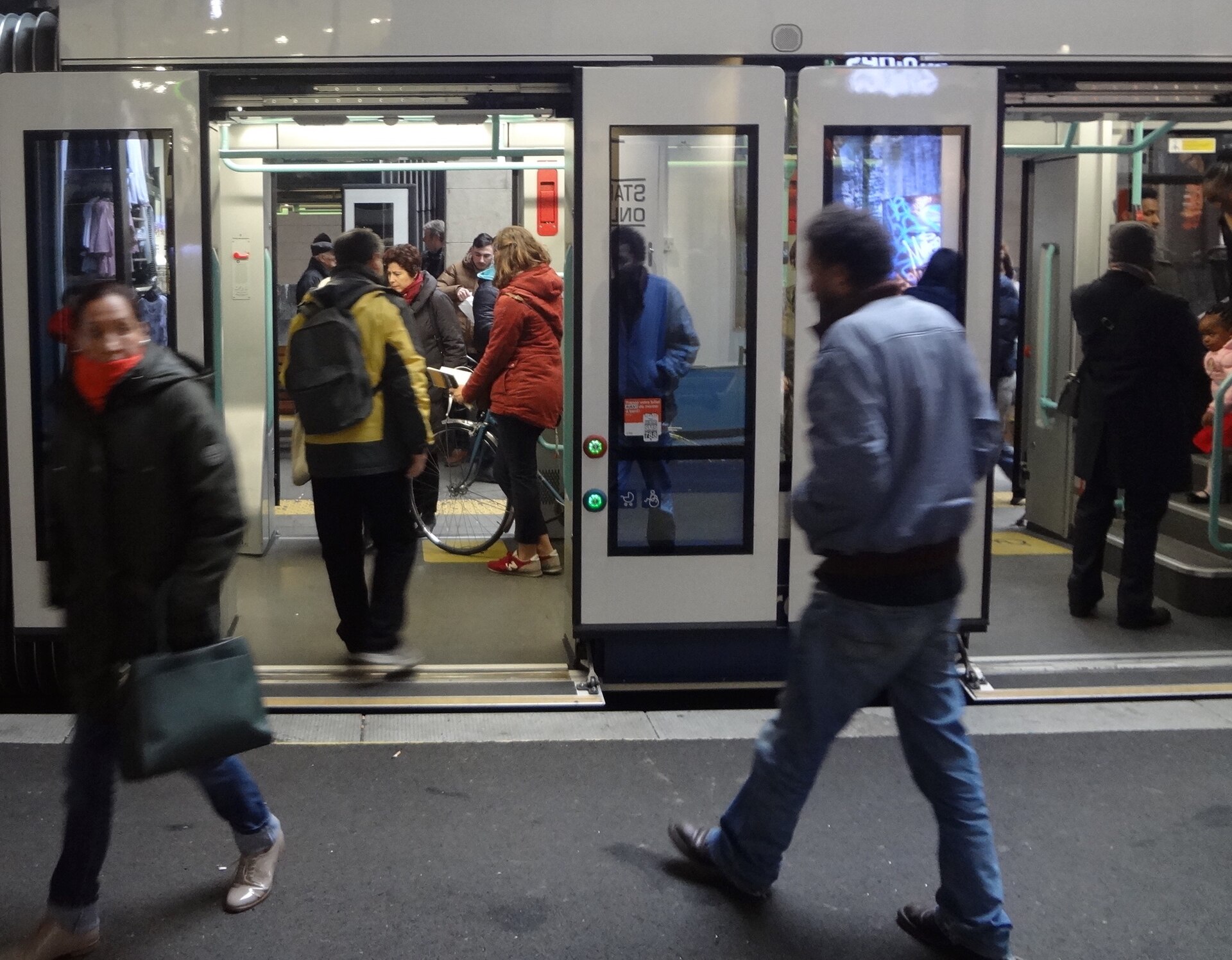 Passengers cross wide open tram doorways at Geneva Cornavin, with low thresholds and stroller and wheelchair symbols beside the buttons.