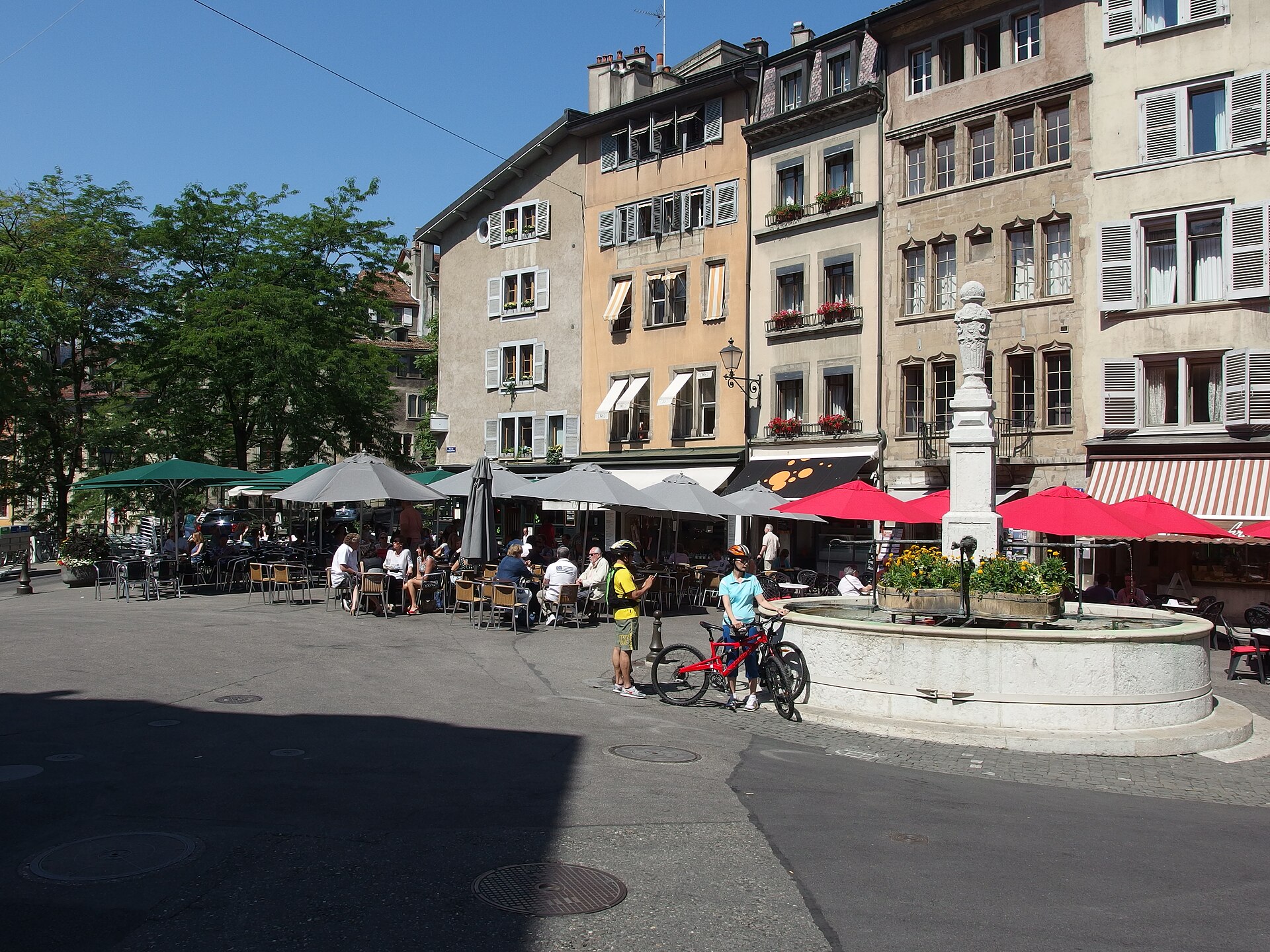 People gather beside the fountain and cafe terraces on Place du Bourg-de-Four in Geneva Old Town.