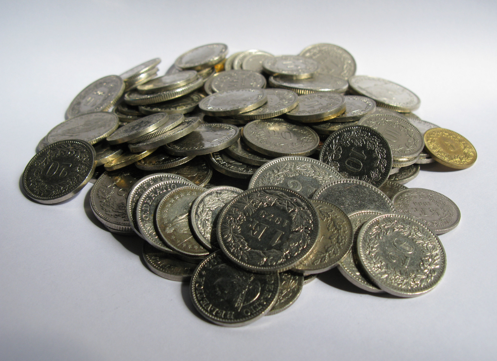 A pile of Swiss franc and centime coins on a white surface, showing different sizes, denominations and engraved designs.