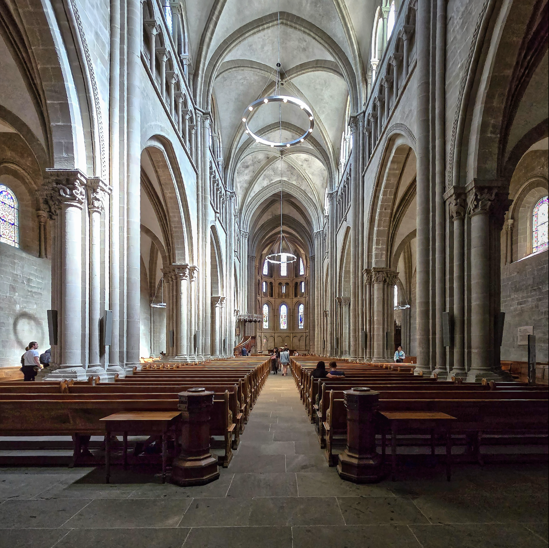 Plain stone columns and ribbed Gothic vaults rise above wooden benches in the nave of St Pierre Cathedral in Geneva.