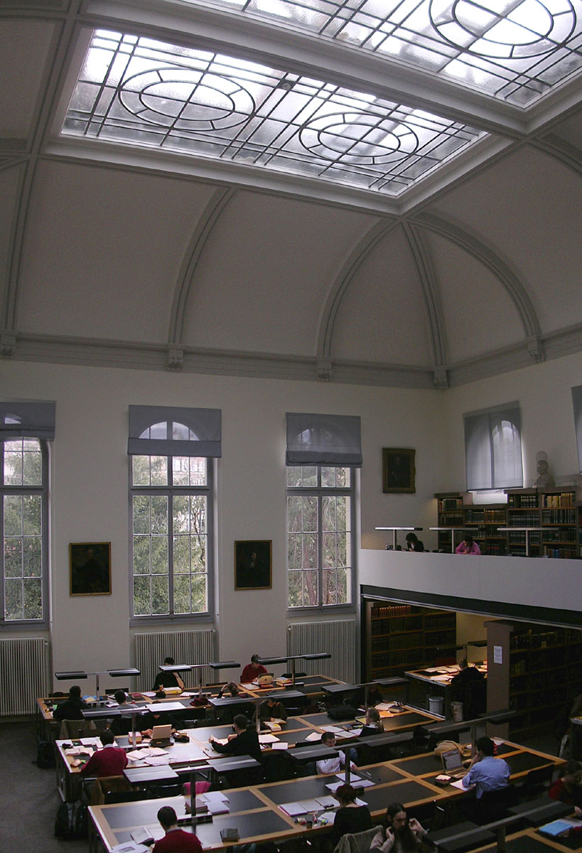 Readers study beneath tall windows and a patterned skylight in the reading room of the Bibliothèque de Genève.