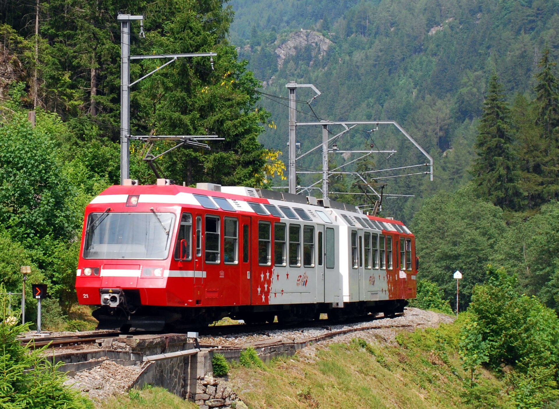 A red and white Mont-Blanc Express train curves through wooded mountain scenery near Le Chatelard-Frontiere on the Swiss border.