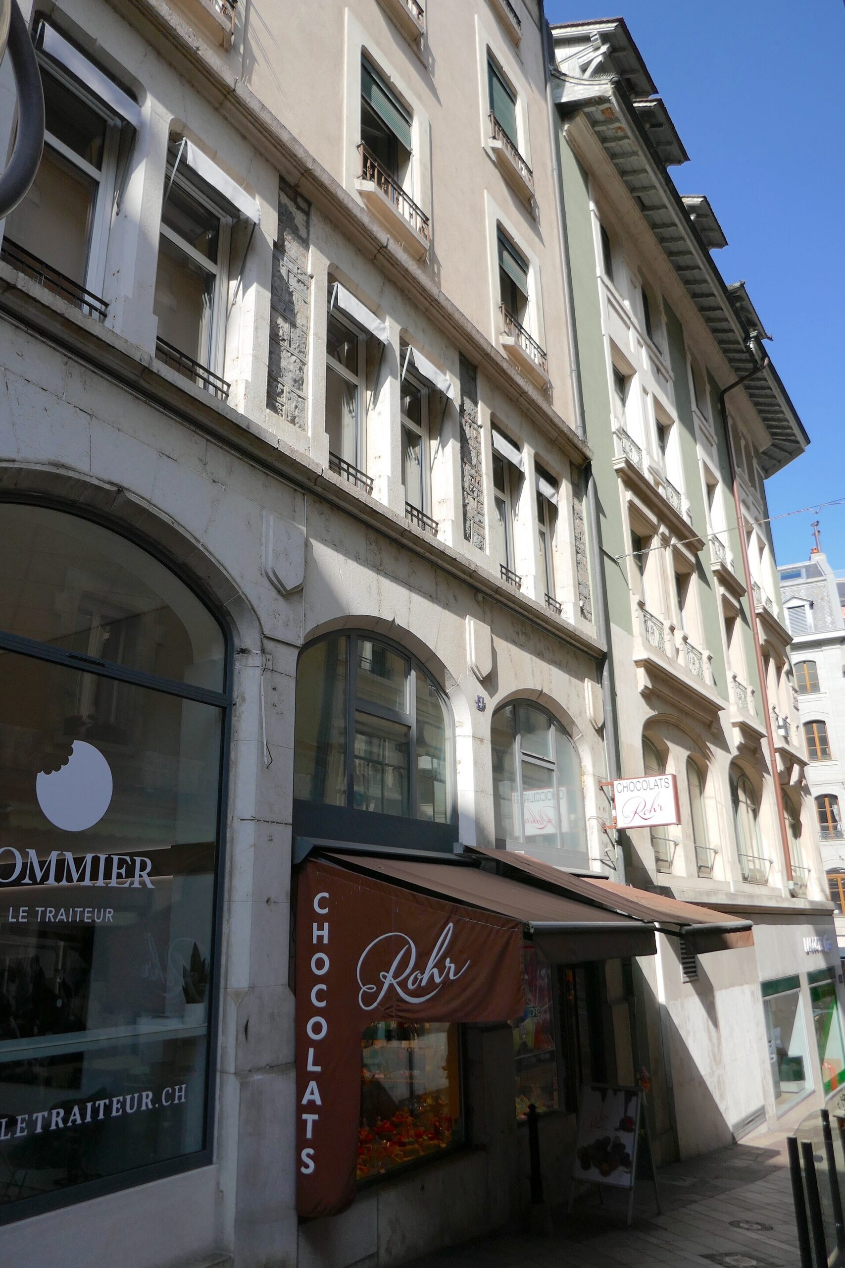 Rohr's chocolate shop window and brown awning sit beneath pale stone buildings on Rue d'Enfer in Geneva.