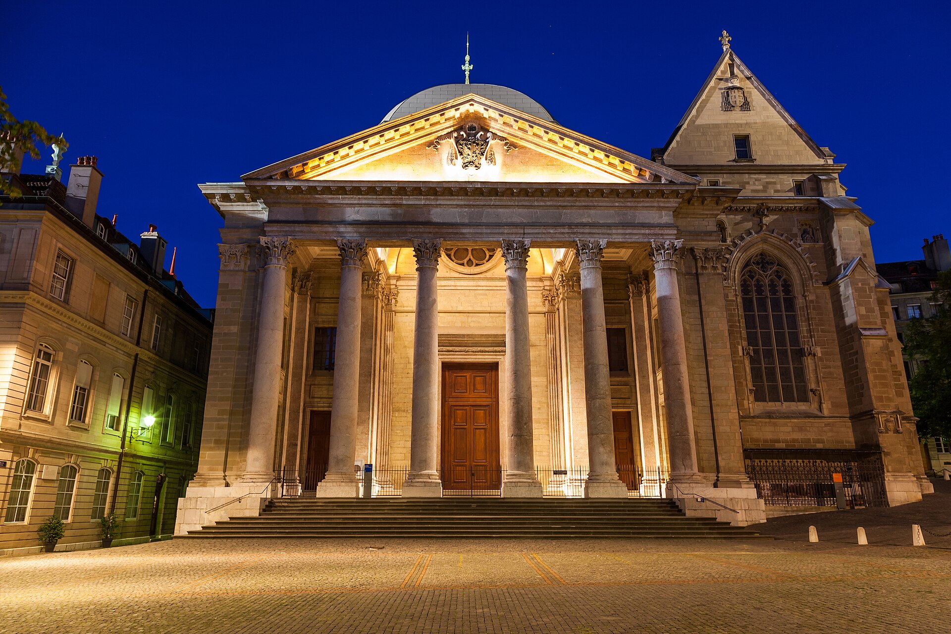 Saint-Pierre Cathedral in Geneva glows above its cobbled forecourt under a deep blue evening sky.