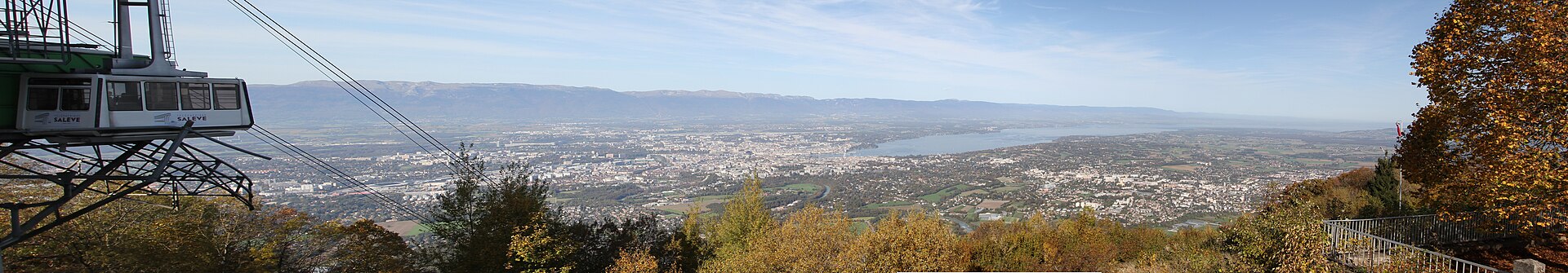 A Salève cable car hangs beside autumn trees above Geneva, with Lake Geneva and the Jura beyond.