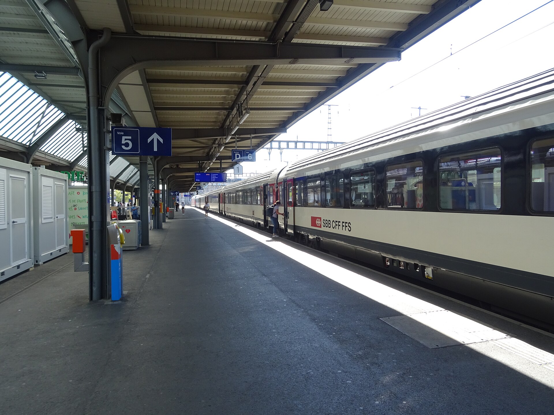 An SBB InterRegio train stands beside a covered platform at Geneva Cornavin, with numbered signs and red carriage doors.
