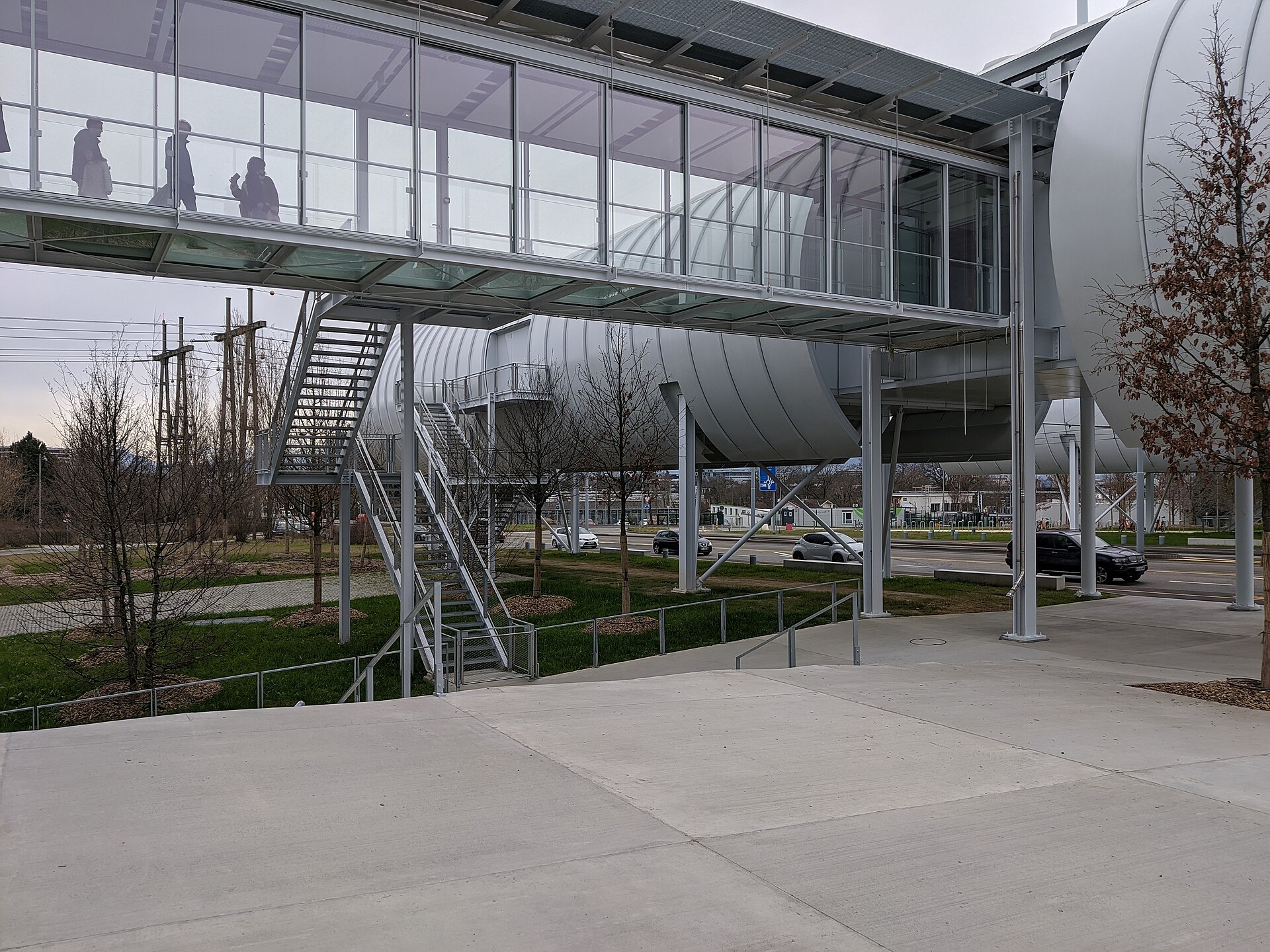 Silver tubular pavilions and a glazed footbridge rise above the courtyard at CERN Science Gateway in Meyrin, with visitors inside.