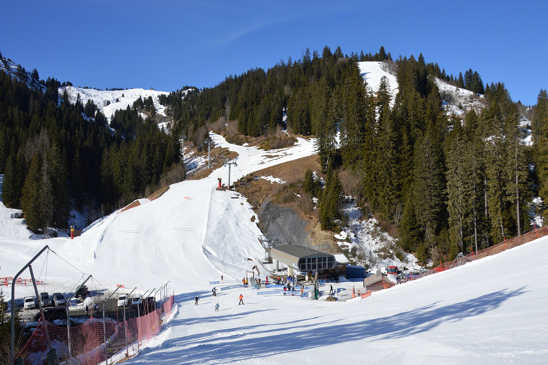 Skiers gather by chairlift base stations below snow-covered runs and forested slopes in the Le Jaillet area of Megève.