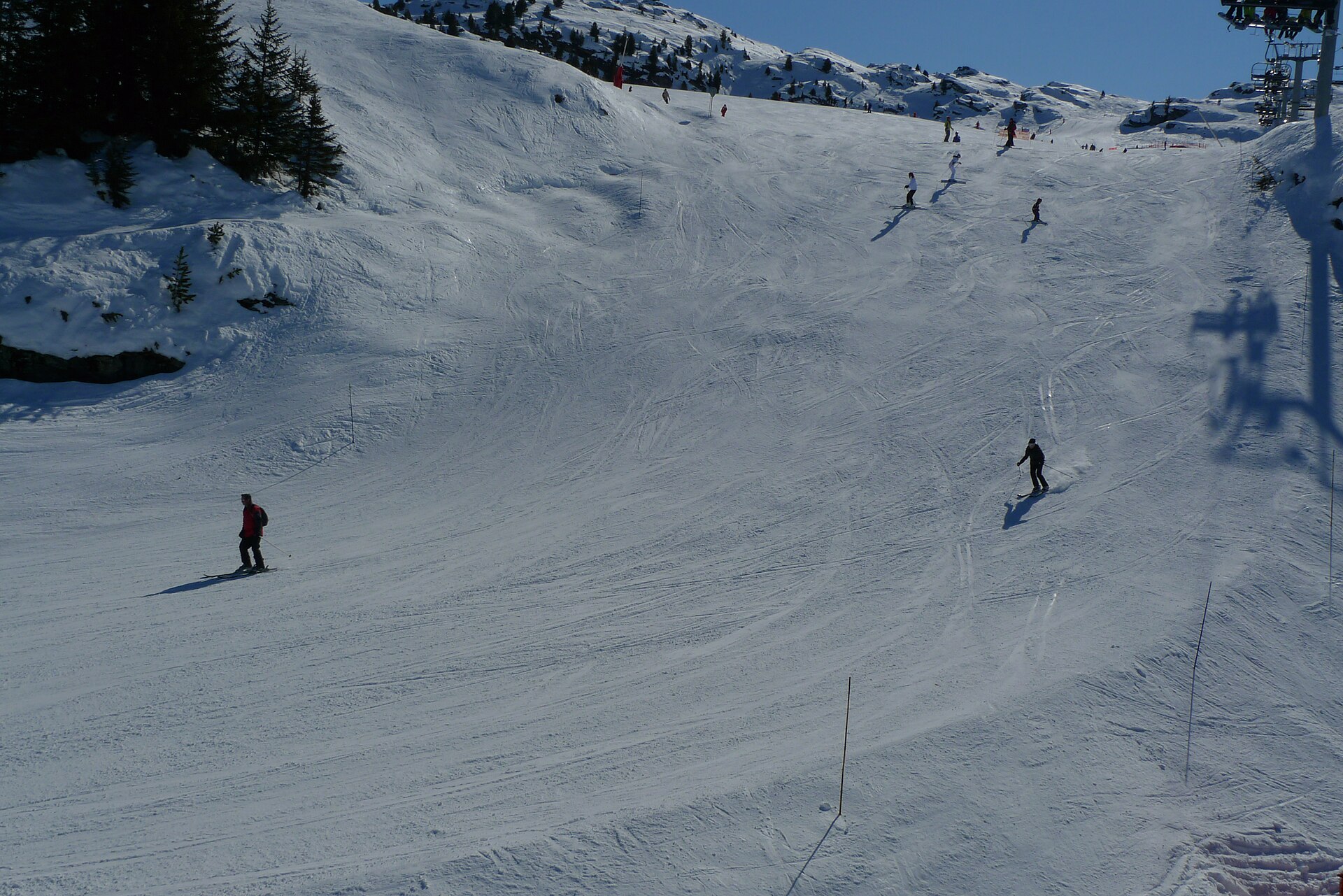 Skiers spread across a broad snowy piste at Ariondaz in Courchevel, with a chairlift overhead.