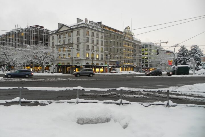 Snow covers the lakeside in front of the watch-shop buildings on Geneva's Quai du Général-Guisan, with a Rolex sign on the roof.