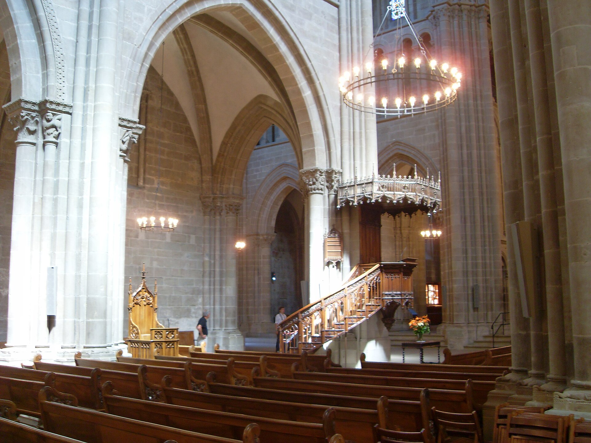 The tall, plain Gothic nave of St Pierre Cathedral in Geneva with rows of wooden pews, a ring-shaped chandelier and a carved wooden pulpit