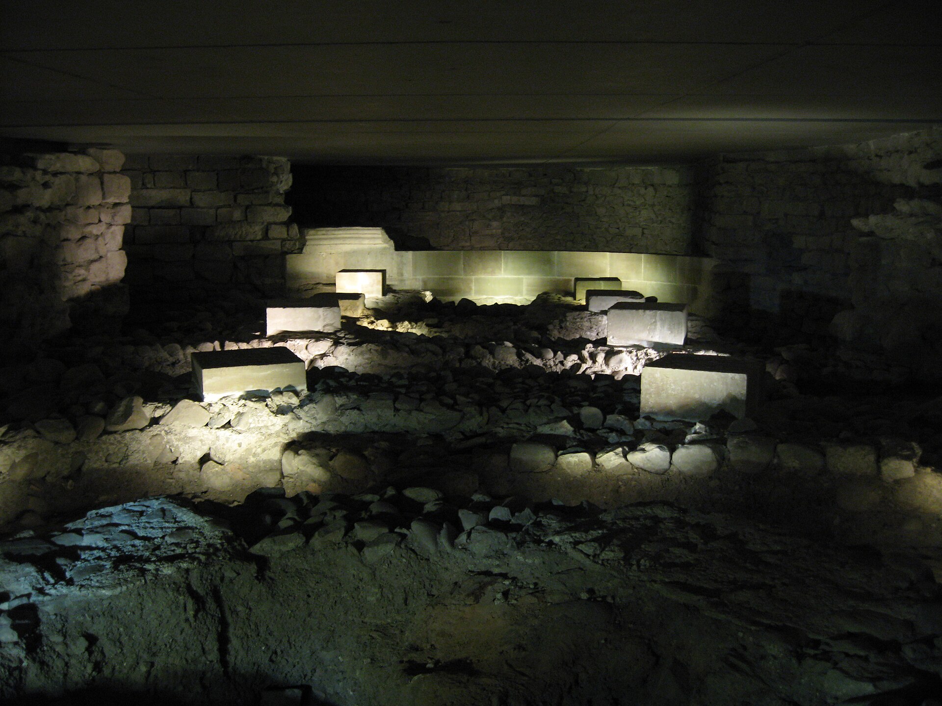 Lit stone foundations and walls of earlier buildings in the dark archaeological site beneath St Pierre Cathedral in Geneva
