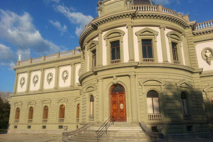 The sunlit Ariana museum in Geneva has a domed central bay, portrait roundels and steps leading to a wooden door.
