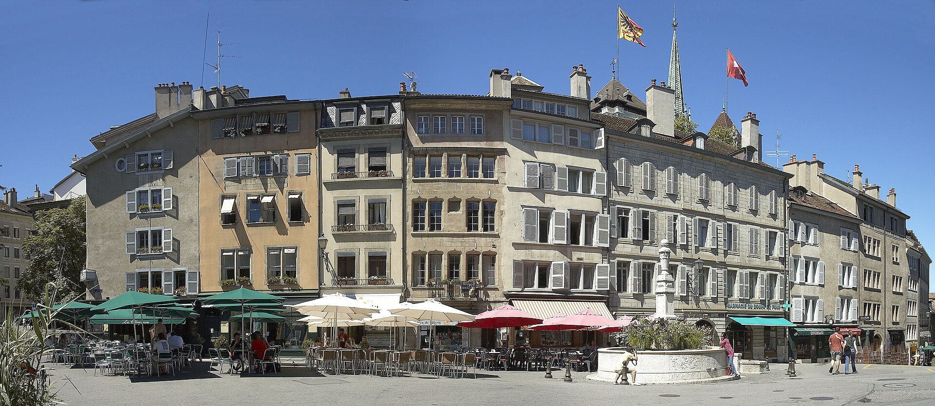 Tall houses and cafe terraces surround the fountain on Geneva's Place du Bourg-de-Four beneath the cathedral spire.