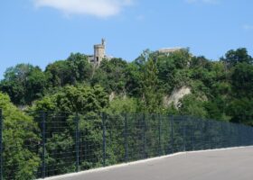 The Tour de Champel rises above wooded Geneva cliffs, viewed from the fenced upper walkway of the Pont des Artisanes.
