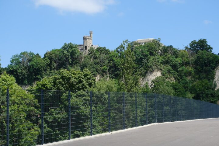 The Tour de Champel rises above wooded Geneva cliffs, viewed from the fenced upper walkway of the Pont des Artisanes.